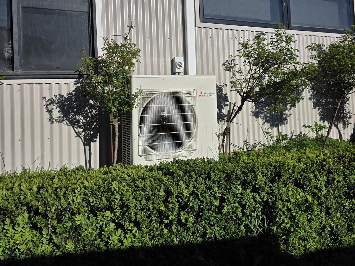 Mitsubishi Electric air conditioner outdoor unit installed on the wall of a shed with an isolator switch above it