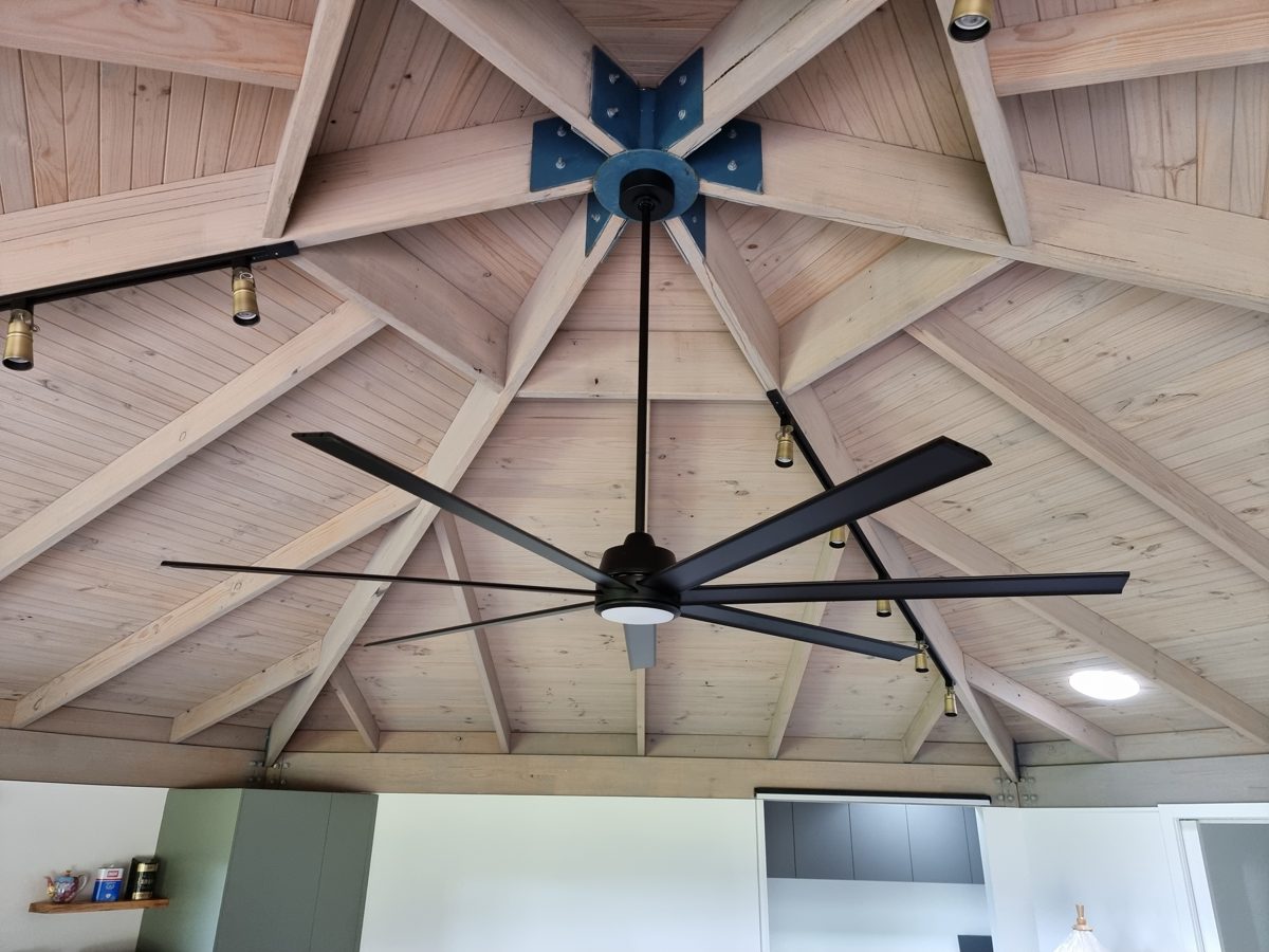 Large black ceiling fan with a light, and brass track lights, in a timber-lined ceiling