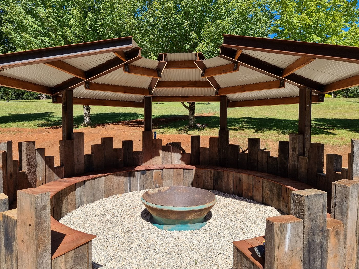 Outdoor timber and steel pavilion with a fire pit and curved bench seating
