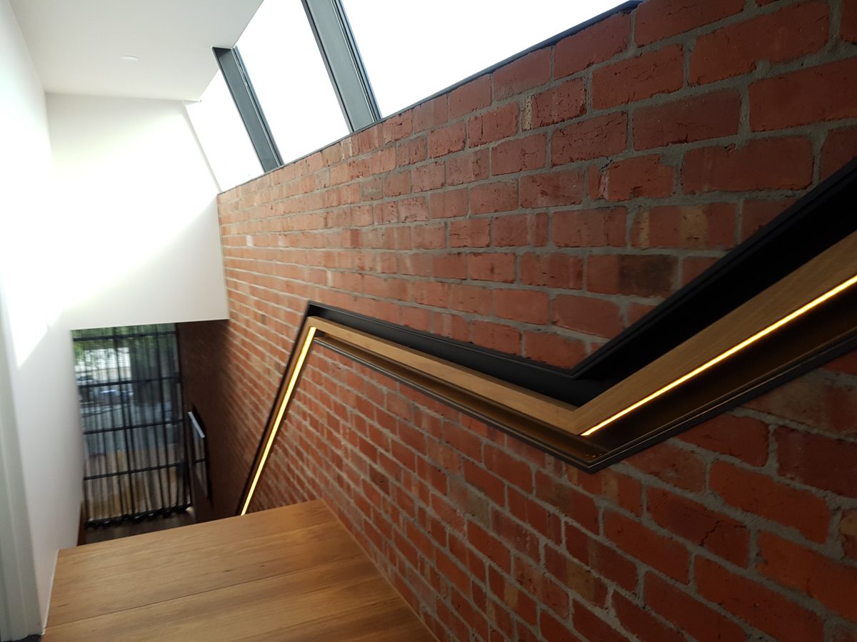 Zigzag timber handrail with an LED strip along a brick wall