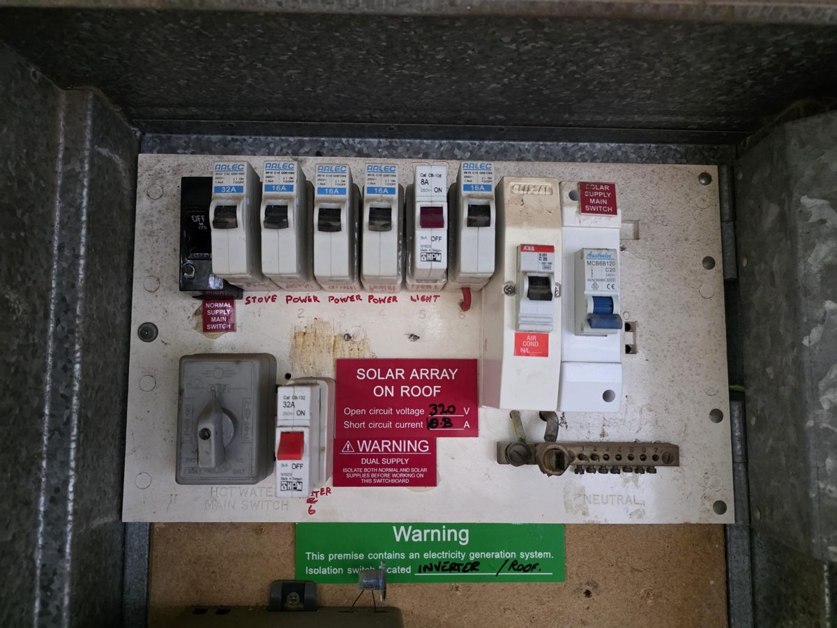 Older switchboard with mixed breakers and solar warning labels