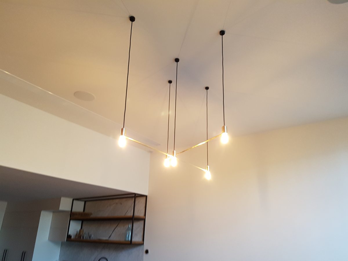 Five pendant lights hanging from black cords above a brass frame