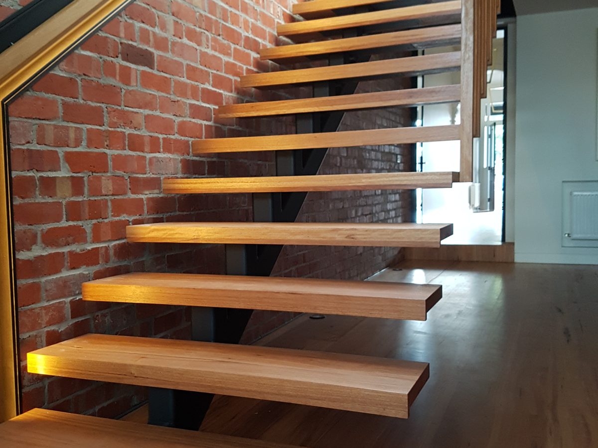 Floating timber stair beside a brick wall with a glowing LED handrail