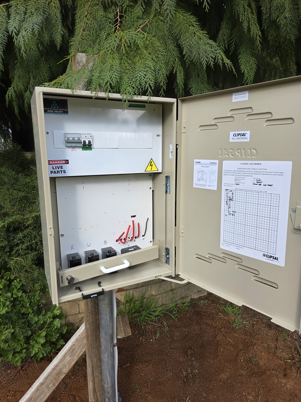 Temporary supply box with the door open showing a main switch, circuit breakers, meter connections and a cable location plan