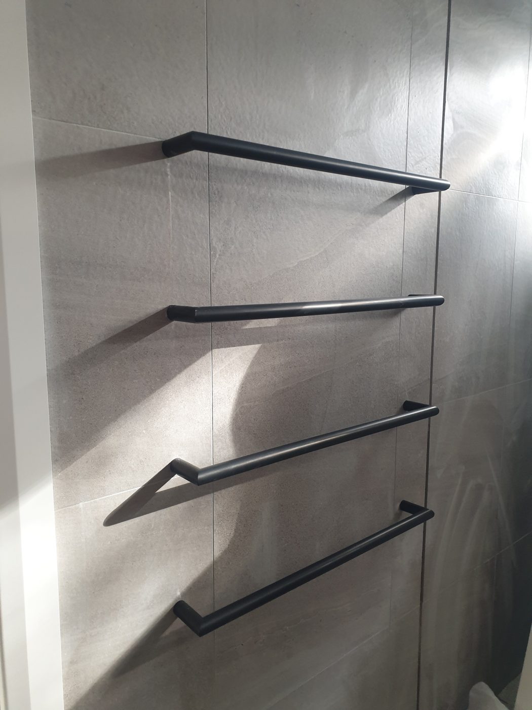 Black electric heated towel rails mounted on a grey tiled bathroom wall