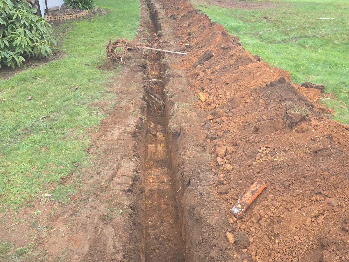 Long trench dug across a lawn with a length of orange conduit beside it
